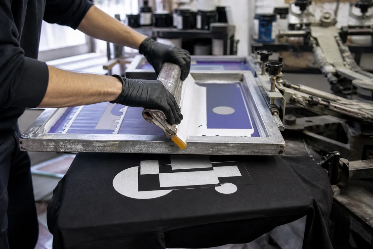 Manual screen printing on a black cotton T-shirt using a mesh screen and squeegee
